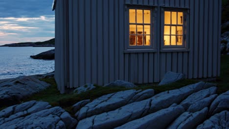 warm light emanating from the windows of a cozy wooden cottage nestled on a rocky coast at sunset, creating a serene and inviting atmosphere