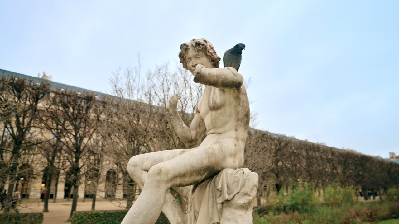 Scultura nei giardini del Palais-Royal nel centro di Parigi, Francia. Persone a passeggio, alberi spogli, cielo nuvoloso