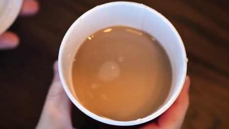 clip taken at coffee shop cafe of a caucasian man taking the lid off of a coffee shop cup with hot coffee or tea in it