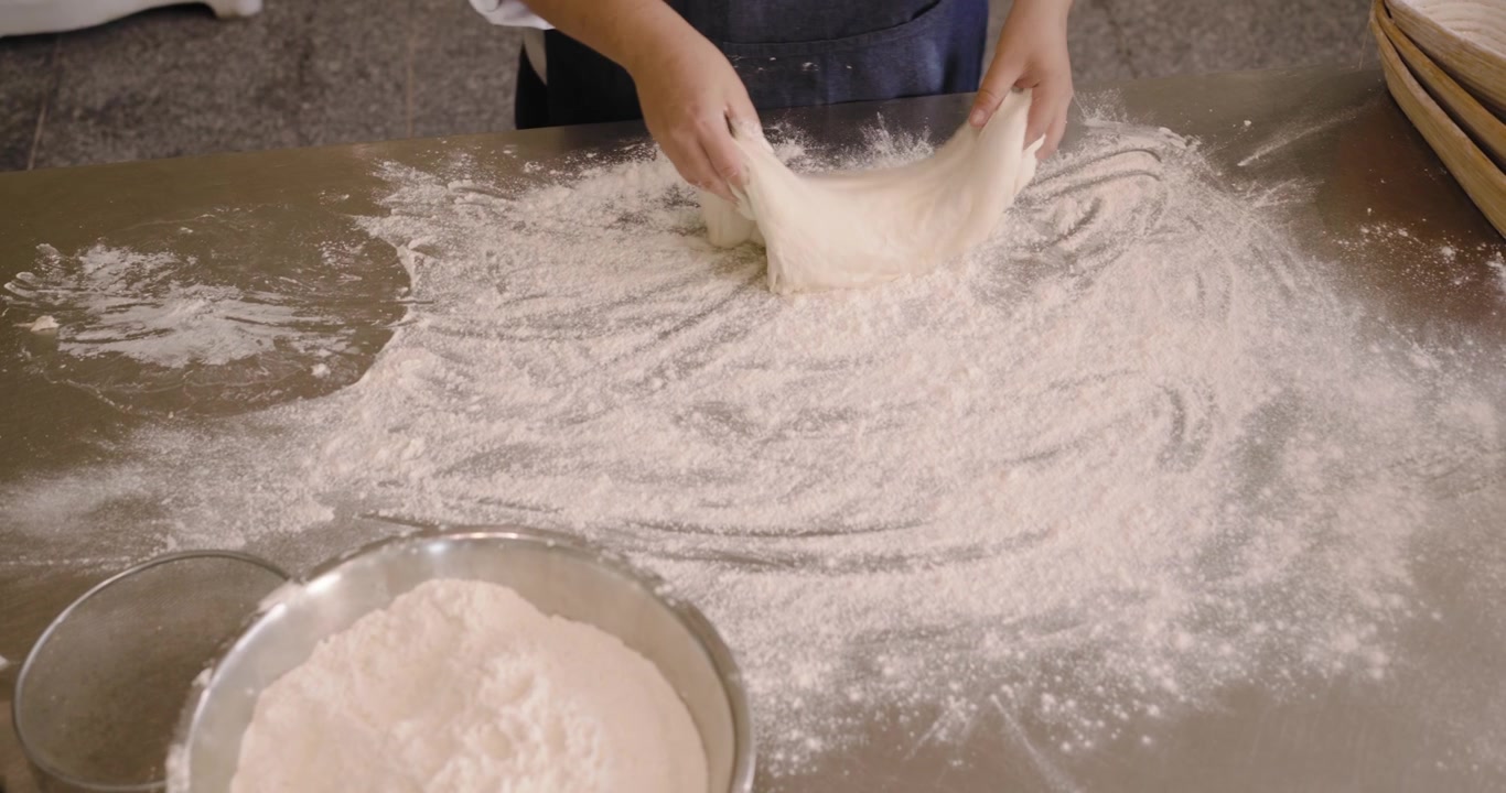 Donna afroamericana con grembiule che cammina con cesti a ciotola, spolverando e modellando l'impasto per la lievitazione in panetteria