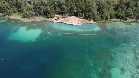 drone aerial footage of a natural lake surrounded by forest in spain with people swimming in it