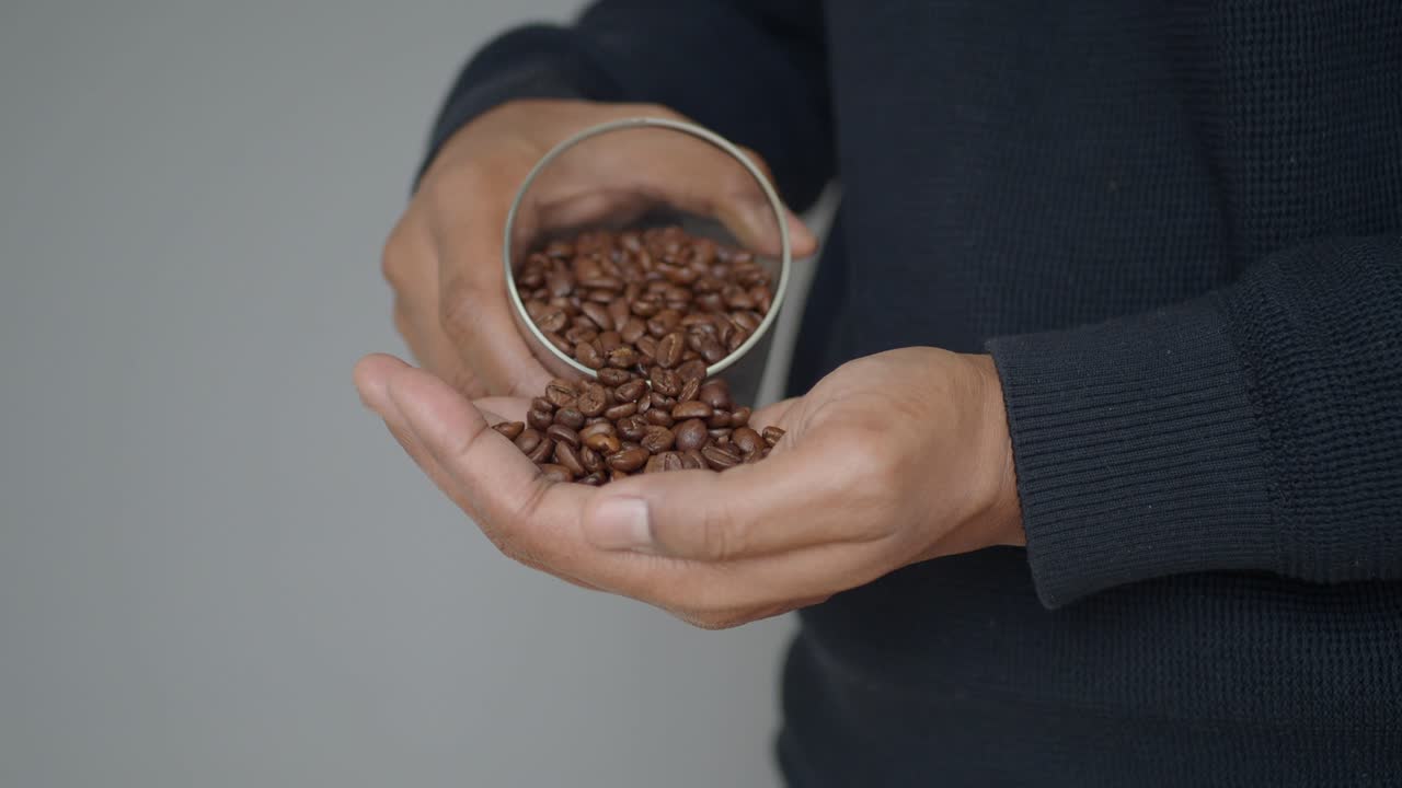 Mani che versano chicchi di caffè tostati da un bicchiere nel palmo