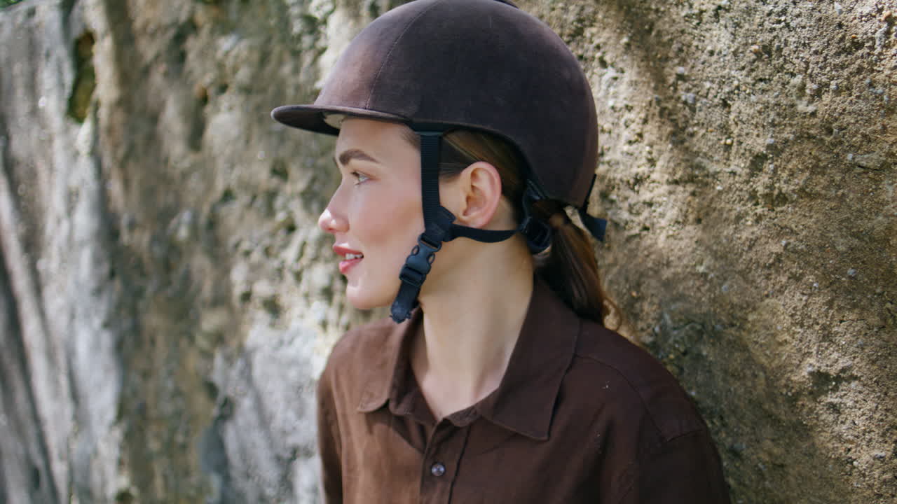 Jockey lady leaning fence at ranch area portrait. Woman in helmet looking camera