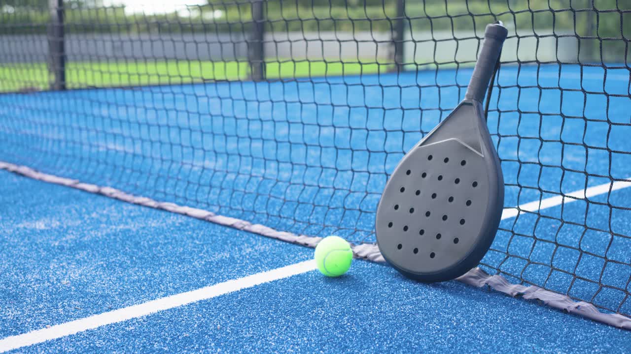 Camera panning right, zooming in to frame black padel racket and neon ball at net line