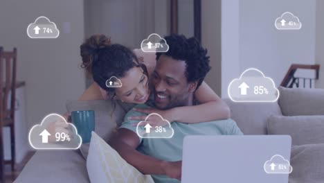 animación de iconos de nubes sobre una pareja afroamericana usando una computadora portátil