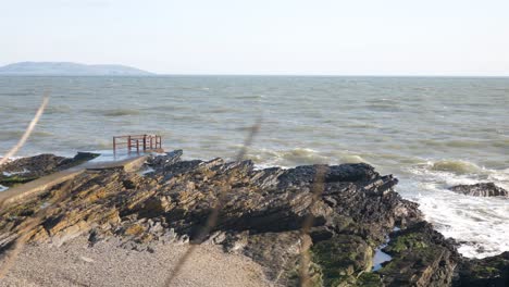 Portmarnock-Beach,-Fingal,-Dublin,-Ireland---A-Picturesque-Sight-of-Waves-Breaking-Against-the-Rocky-Coastline---Wide-Shot