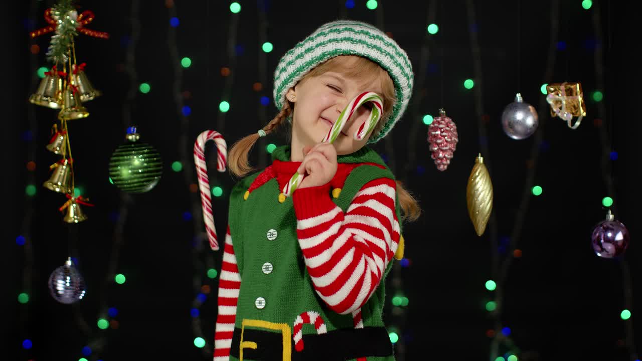 Kid girl in Christmas elf Santa Claus helper costume with candy cane lollipop joyful smiling