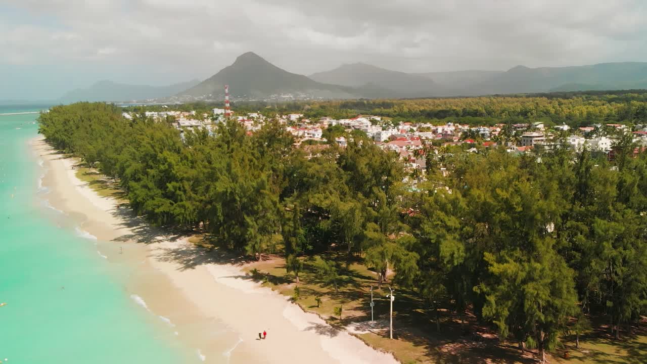 olas rompiendo en la arena blanca de la playa de flic en flac y edificios enclavados en medio de frondosos árboles verdes