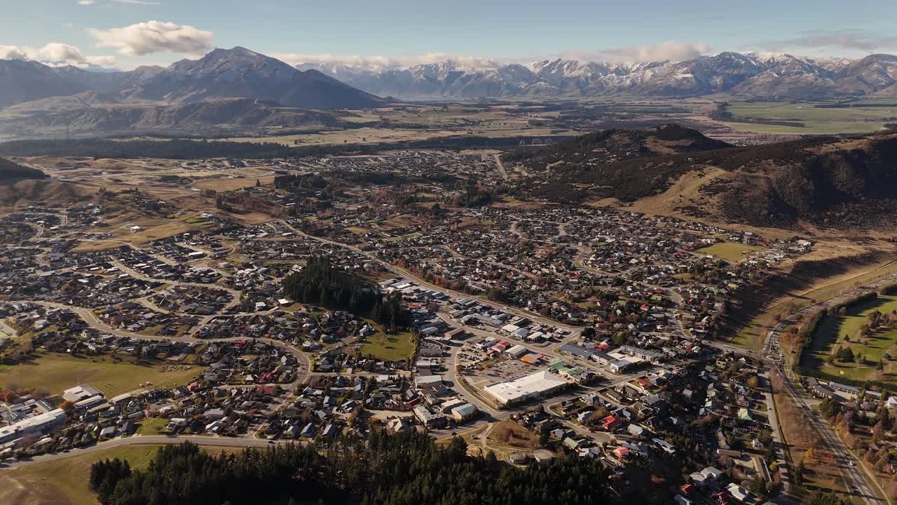 High aerial establishing shot of Wanaka town nestled in valley with mountain range in background, New Zealand