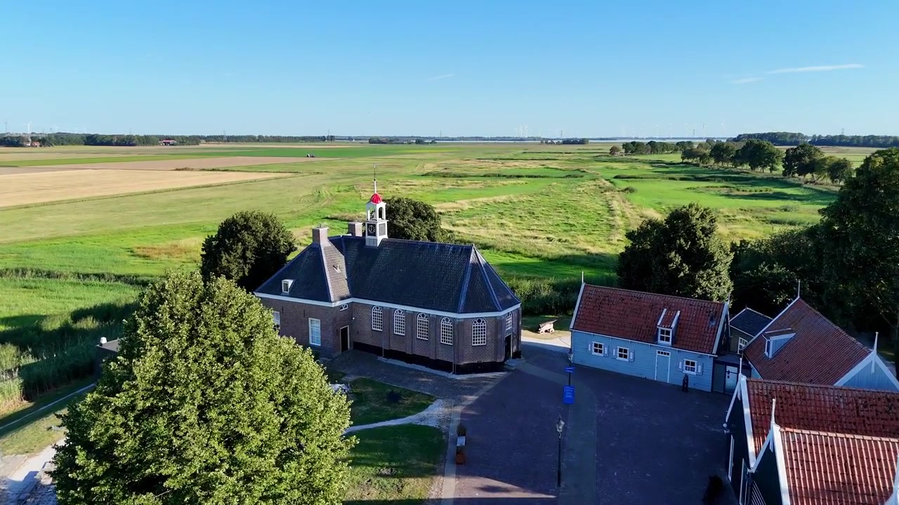 Uma vista panorâmica de drone capturando a histórica antiga ilha de Schokland, nos Países Baixos, num dia claro e ensolarado. Voando sobre a entrada em direção à igreja, revelando o canhão. Viajante solitário