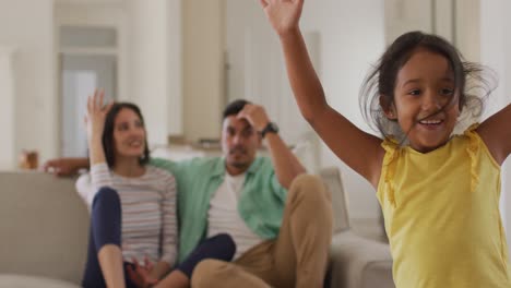 Tired-hispanic-parents-sitting-on-sofa-looking-at-dancing-daughter