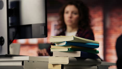 pila de libros en el escritorio de la oficina de inicio frente a la mujer trabajando, primer plano