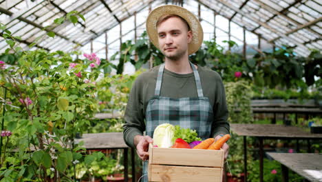 farmer holding a wooden crate of fresh vegetables in a greenhouse