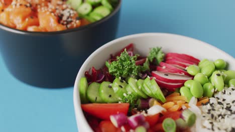 composition of bowls with rice, salmon and vegetables on blue background