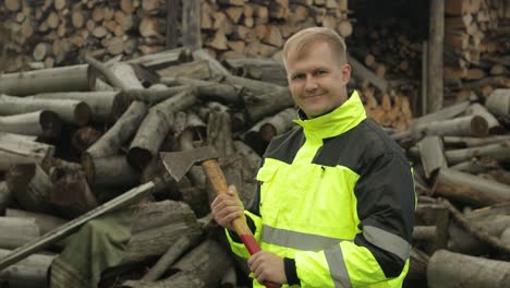 lumberjack in reflective jacket. man woodcutter with small axe. sawn logs, firewood background