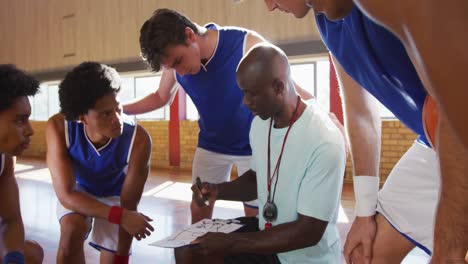 equipo de baloncesto masculino diverso y entrenador en grupo discutiendo tácticas de juego