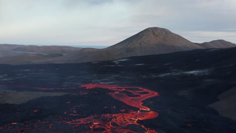 Molten-lava-river-in-Meradalir-valley-with-Stóri-Hrútur-mountain-in-background,-aerial