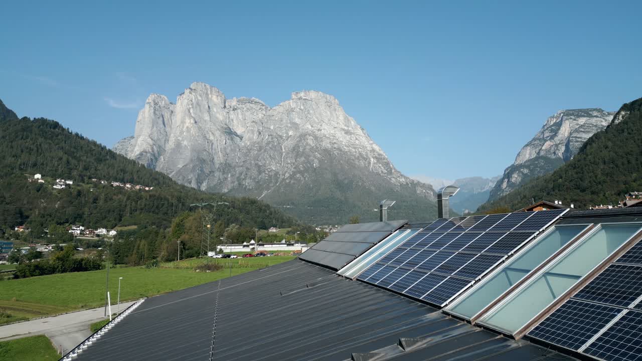 Průmyslová továrna se solárními panely na střeše pro obnovitelnou energii, v pozadí hory.