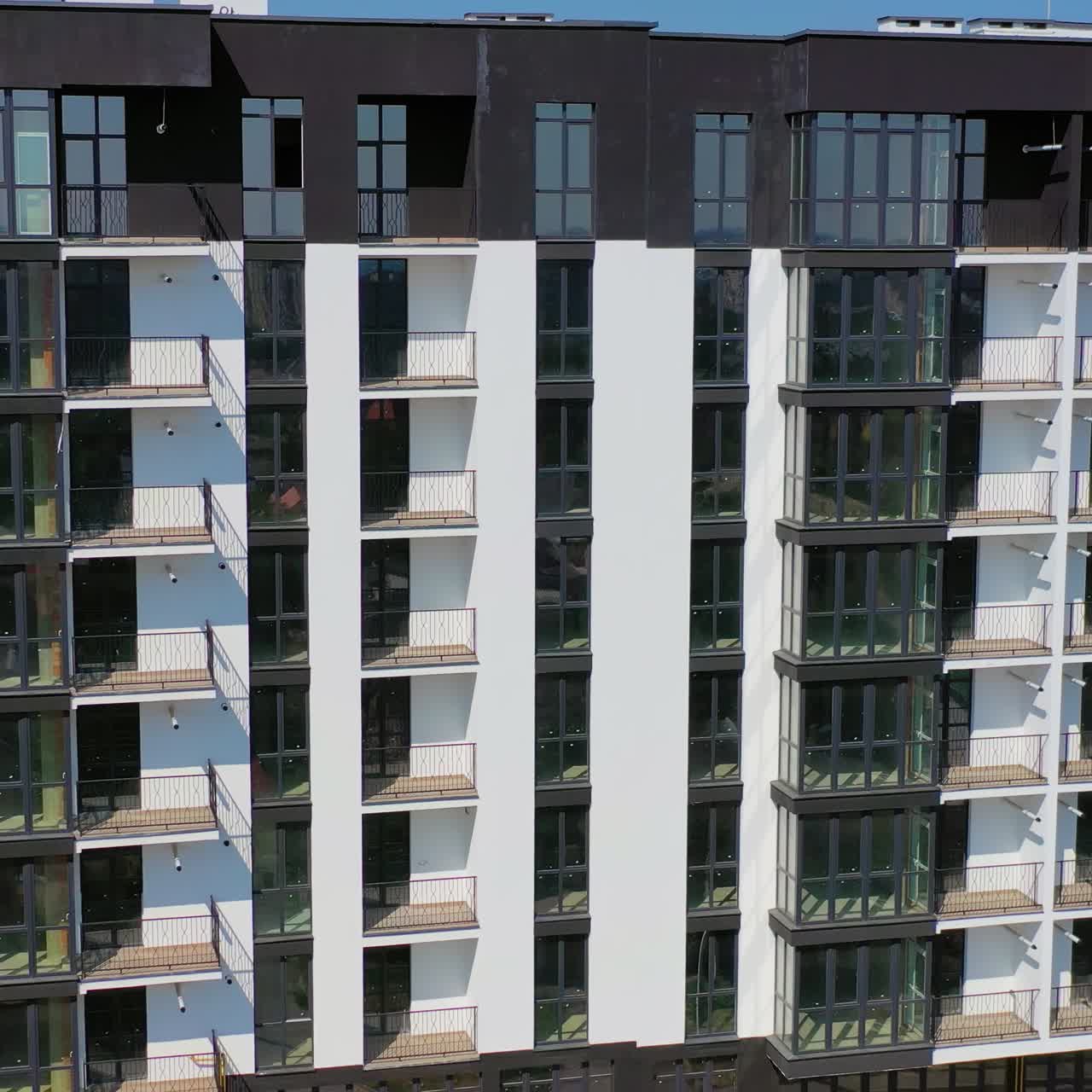 Facade of new block of flats. Modern design of black and white multi storey architecture in the city. Beautiful high-raise building with balconies and tall windows.