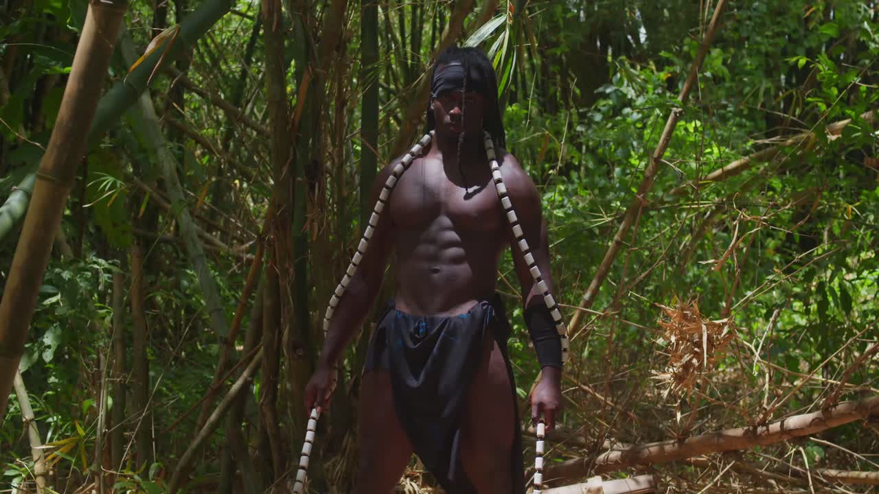 A muscular, dark-skinned man, expertly portraying Tarzan in costume, is immersed in a woodland setting.