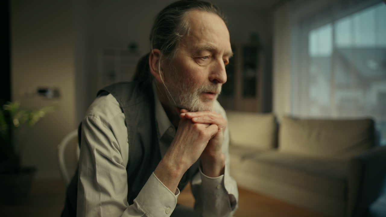 Thoughtful Elderly Man Resting Chin on Clasped Hands Indoors