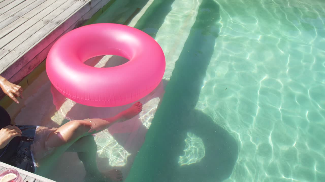 Holding pink ring on pool-deck African American woman steadying lowering to float, copy space