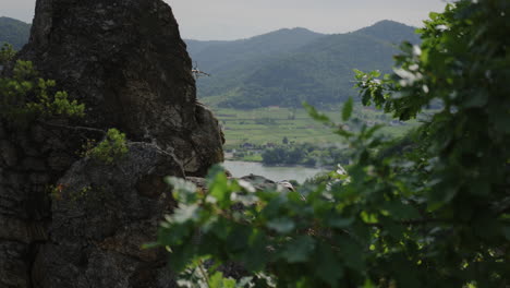 athletic-man-climbing-mountain,-close-up-hand-reaching-rocky-grip,-bouldering,-hazy-landscape-in-background,-fit-male-free-climb,-placing-hands-to-climbs-high,-altitude,-slow-motion,-cinematic-shot