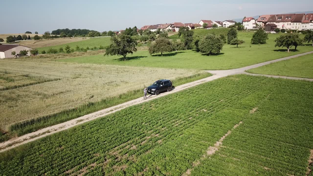 푸시 아웃 드론 공중 보기:한 남자가 스위스 시골 들판에서 xc90 suv 볼보 자동차 앞에서 드론을 운전합니다.