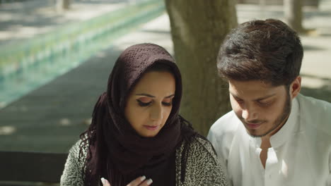 Romantic-muslim-couple-sitting-on-bench-in-park,-holding-hands.