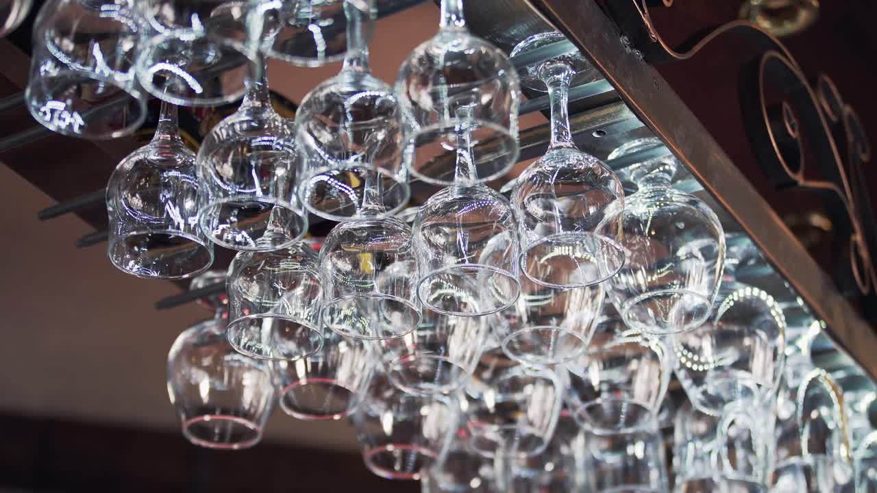 Metal rack with small clean glasses for alcohol in rows on the background of a bar. Crystal glasses hang upside down