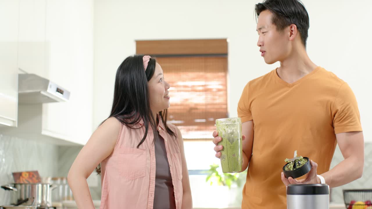 คู่รักชาวเอเชียกำลังดูชายคนหนึ่งตรวจสอบเนื้อสัมผัสของสมูทตี้สีเขียวสดในถ้วยและชามบนเคาน์เตอร์