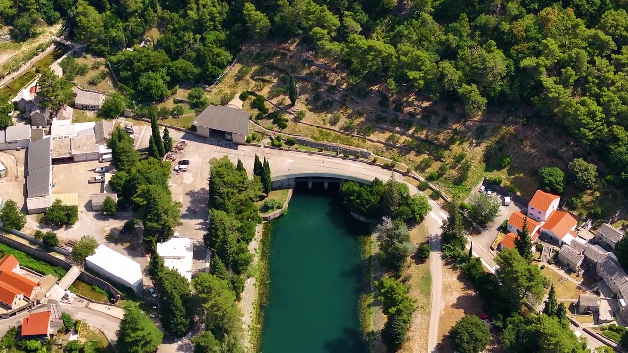 Infrastruttura per l'energia rinnovabile situata in una valle fluviale. L'elettricità viene generata e trasmessa dall'impianto. Alberi ed edifici circondano l'area.