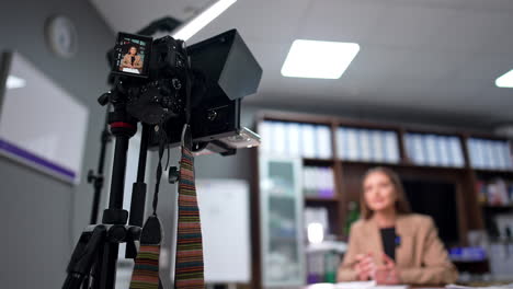 professional camera with display set on tripod footages a woman. low angle view. female blogger creates content for her blog or vlog. blurred backdrop.