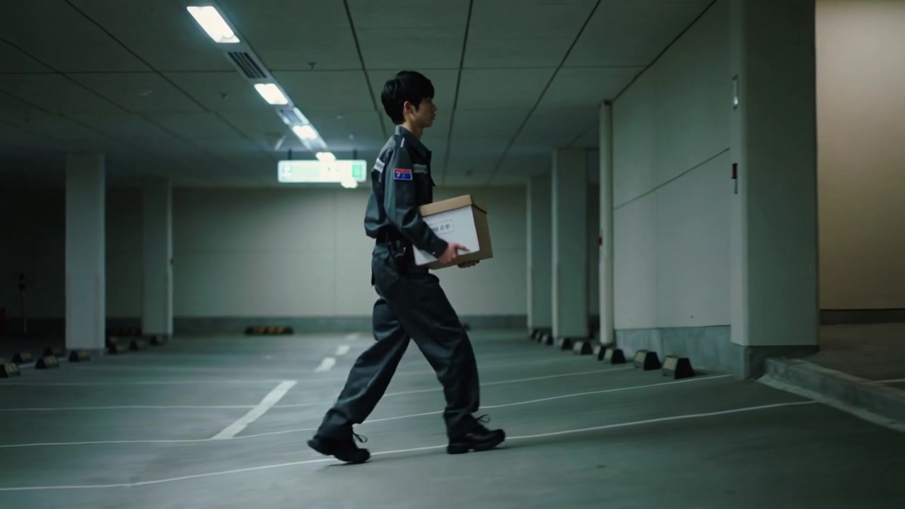 Walking uniformed man carrying labeled box across parking garage, delivering to recessed doorway