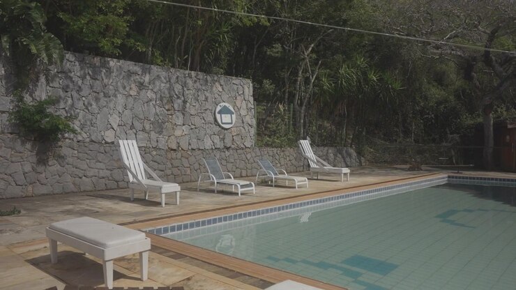 Still pool water reflecting sun loungers and a stone wall behind
