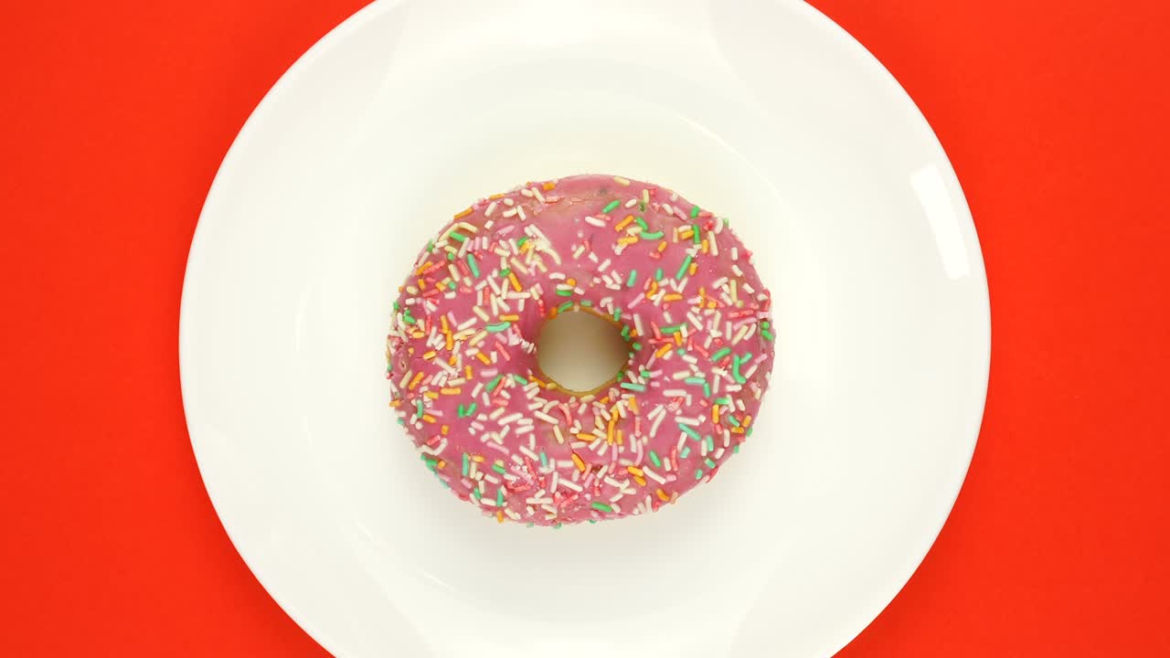 brillante y colorido salpicado rosquilla primer plano disparado girando lentamente en una placa blanca de color. vista superior. bucle sin costuras.