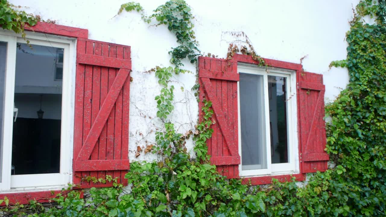 enredaderas que crecen sobre puertas francesas rojas en ventanas construidas en la casa con cámara panorámica a través de la escena