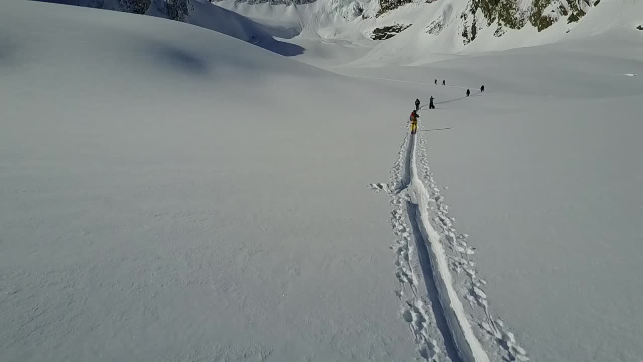 drone que se eleva verticalmente mientras los esquiadores de backcountry suben a la pista de skintrack