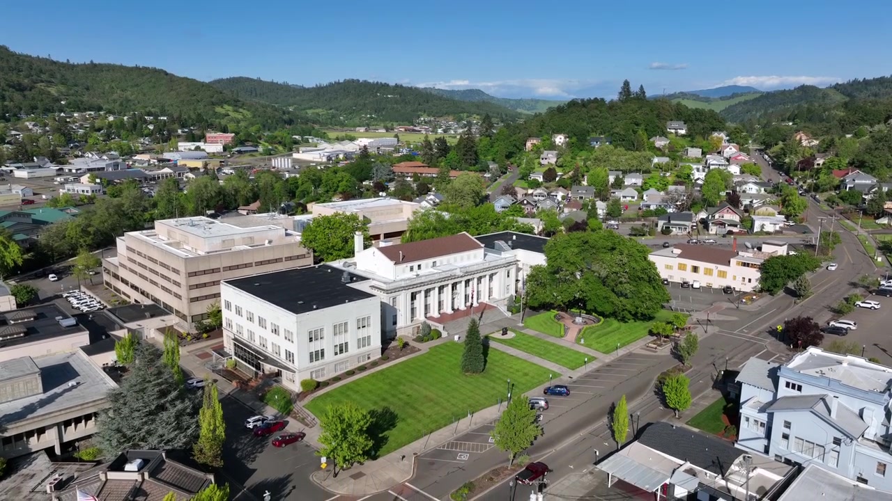 Storico tribunale con facciata a colonne e prato verde curato che domina il centro di Roseburg, circondato da quartieri residenziali e lussureggianti colline boscose, Oregon, USA. Ripresa aerea in discesa con drone