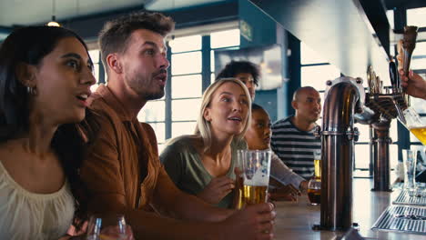 multi-cultural group of friends in sports bar celebrating as they watch game on tv