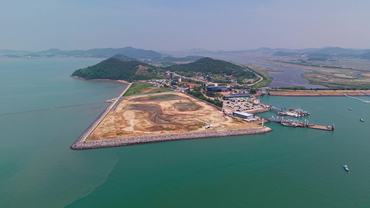 Cảnh quay trên không tiếp cận Cảng Tando với làng chài ven biển, những ngọn đồi xanh, khu vực lấn biển, cầu cảng và những chiếc thuyền neo đậu bên cạnh bãi triều ở Hàn Quốc.