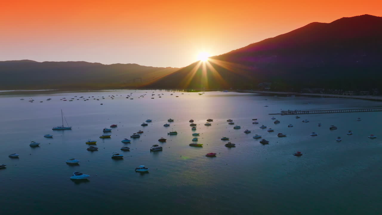 Bright orange sky over the Lake Tahoe at sunset. Numerous boats enjoying the sundown view from water. Aerial view.