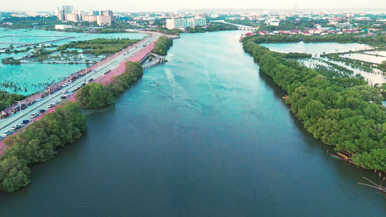 Scenic drone footage of a wide river with mangroves, traffic on a road, and city skyline in the Philippines. Great for travel, transportation, and urban development projects