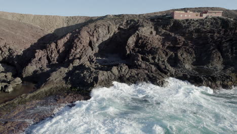 toma aérea a lo lejos de una joven que está sobre una roca frente a la costa y donde se ven las fuertes olas