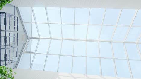 low angle rotating shot of the glass ceiling in the hospital / building / mall/ supermarket. big white building with sun rays coming out of windows.