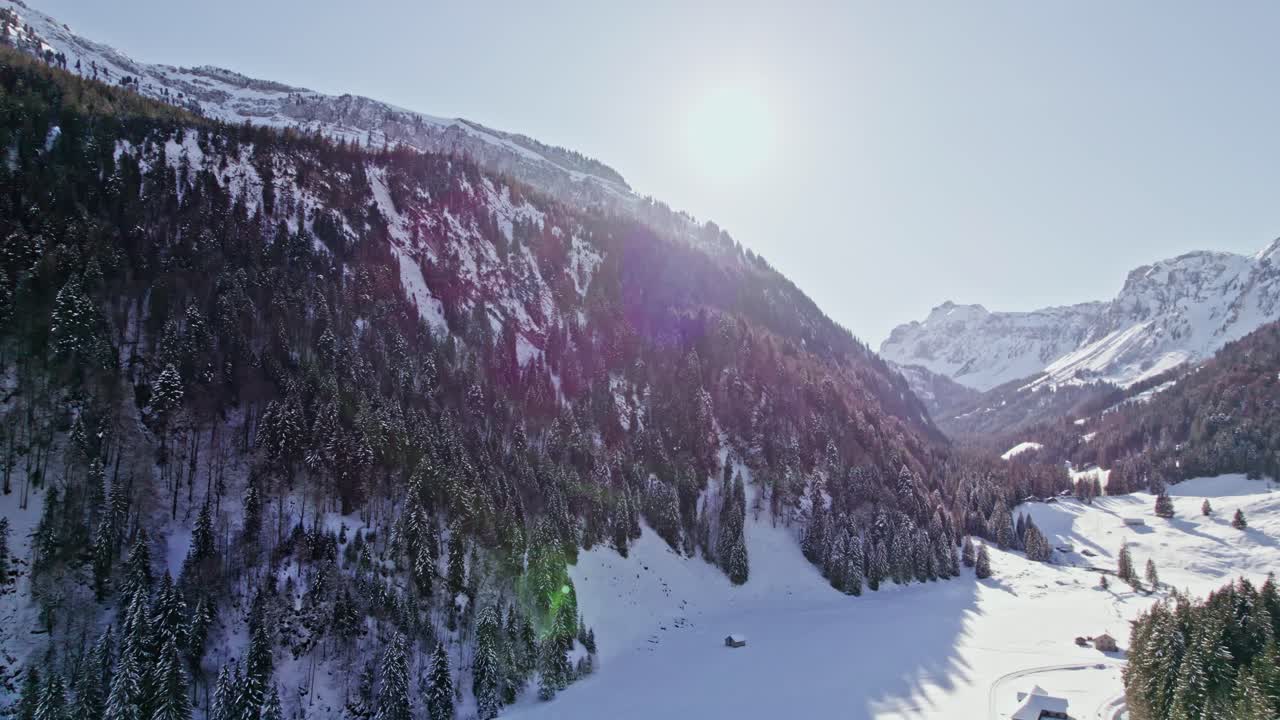 Winter scenic view of Swiss alps. Sun rays behind the peaks with evergreen forest covered in snow. Obersee Glarus Nord, Switzerland