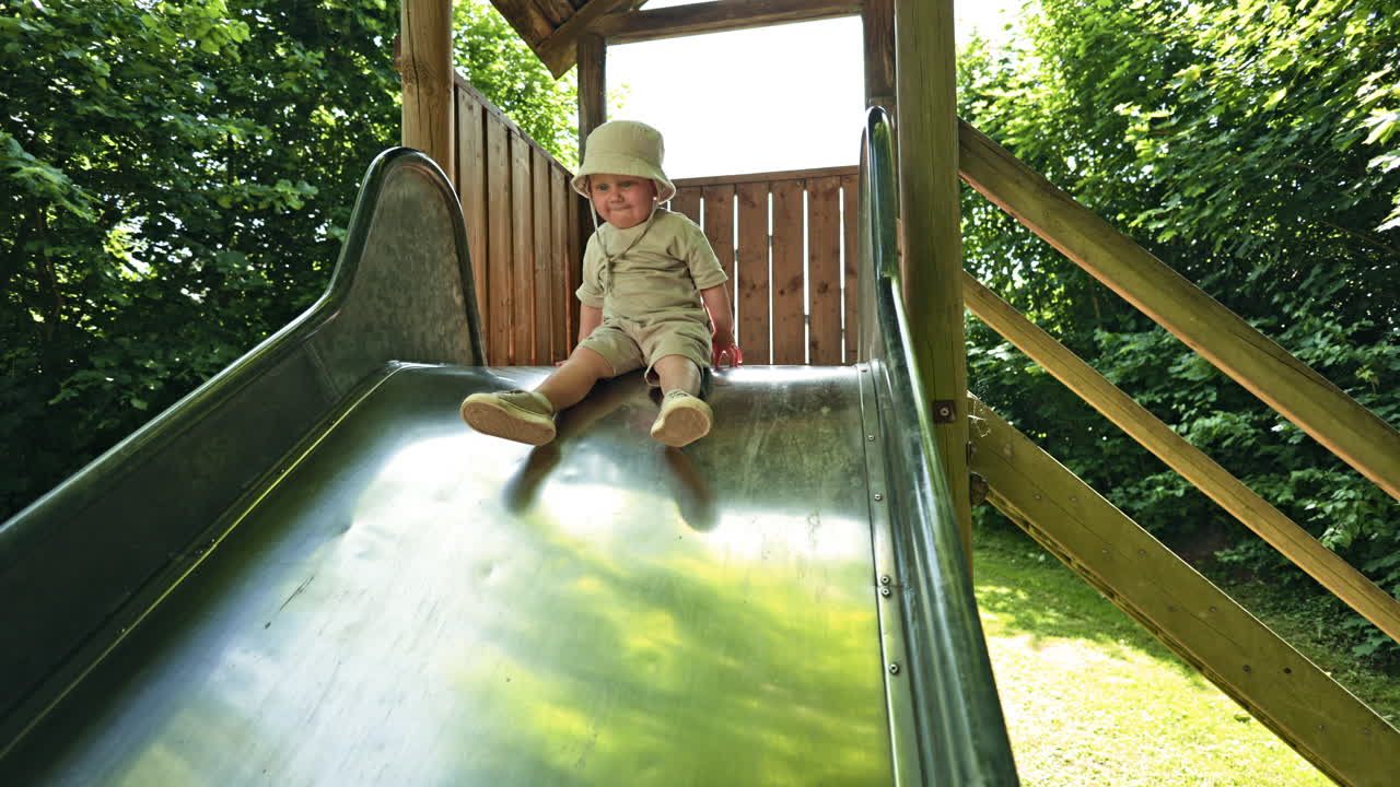 An energetic boy plays on a playground and slides down a slippery slide. A child slides down a high slide. Children's swing outdoors