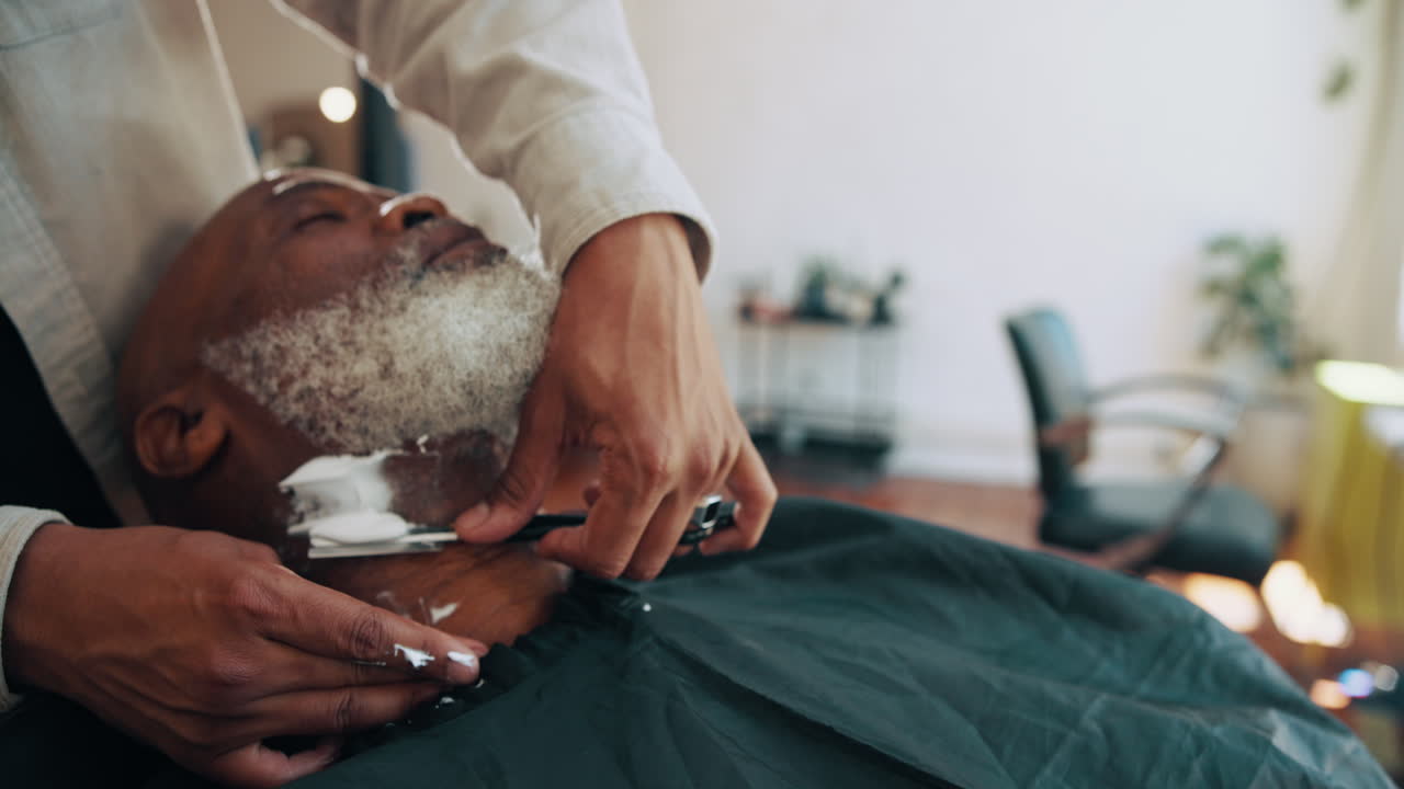 Barber Shaving Senior Man's White Beard with a Straight Razor