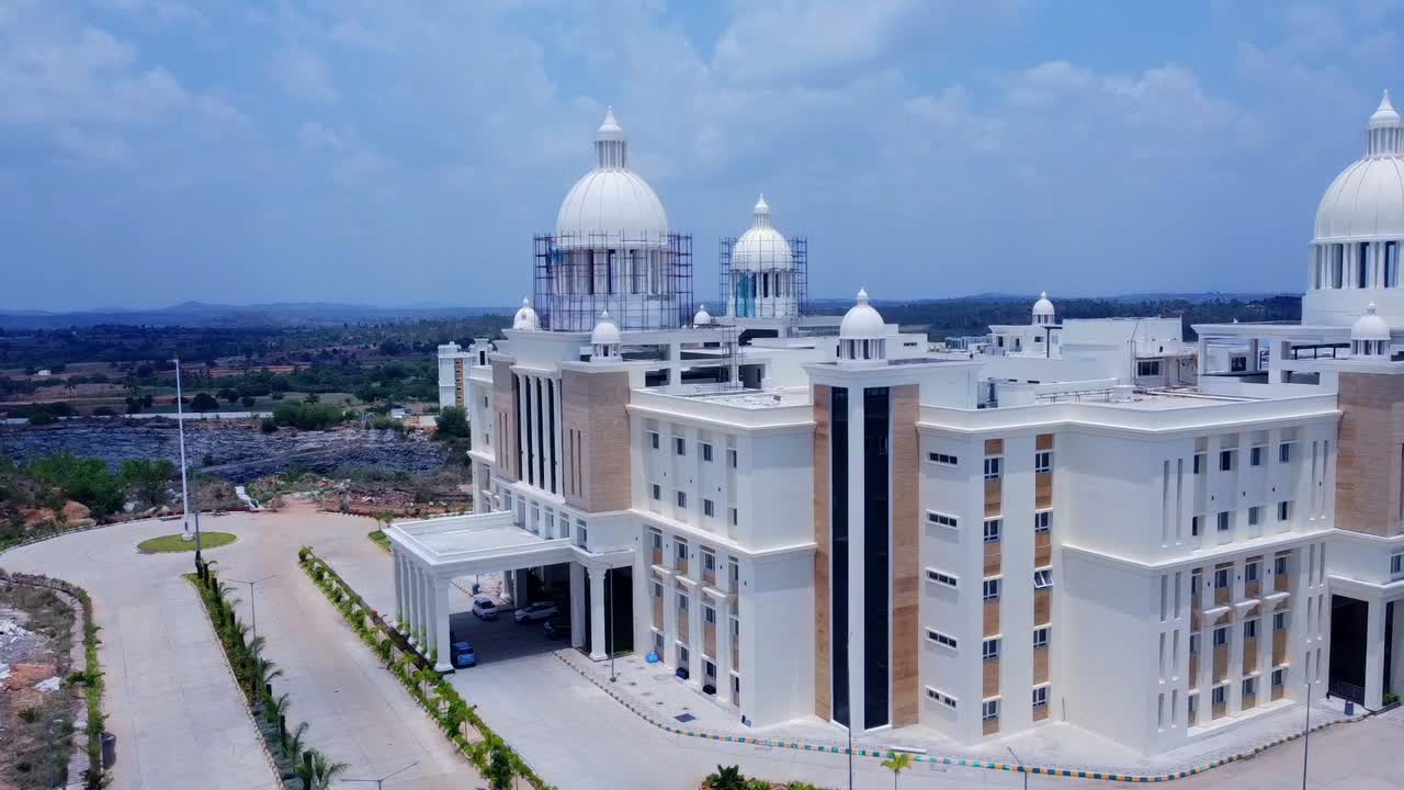 Aerial shot trucking sideways past a massive neo-classical building under construction in India. Scaffolding on the grand domes shows the final stages of development against a bright blue sky