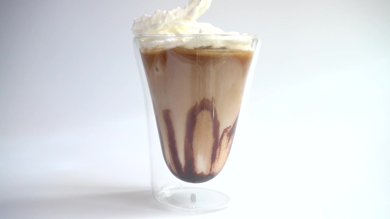 Preparación de bebida de café con hielo, leche, café, nata y sirope de chocolate. Cámara lenta.